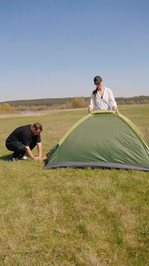 Young couple assembling a camping tent together in a sunny field Видео 344602413