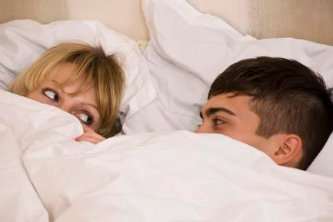 A young couple in bed with the duvet pulled up to their eyes Stock Photos