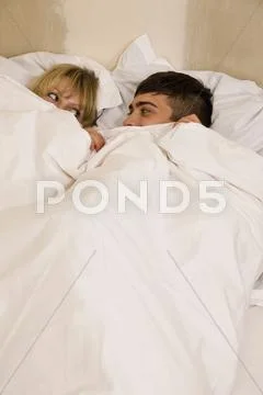 A young couple in bed with the duvet pulled up to their eyes Stock Photos