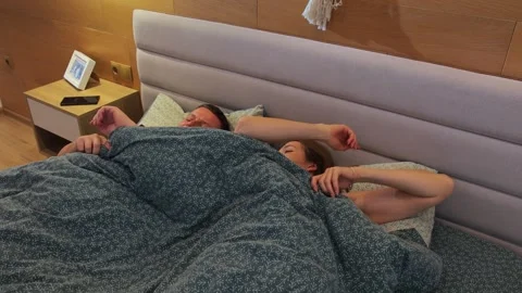 A young couple in bed wake up in the morning. They open their eyes and say hello Video stock 292906826