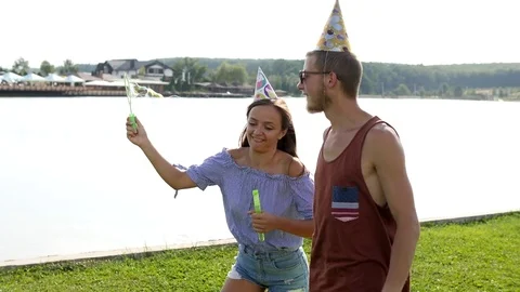 Young couple blowing soap-bubbles on the lake background. Stock Footage 80657425