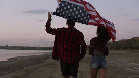 Young couple both in red plaid shirts are running on the seashore with american Stock Footage 91209545