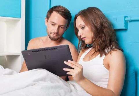 Young couple browsing internet on tablet computer while sitting in bed Stock Photos