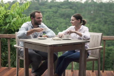 Young couple chatting by table drinking coffee on terrace with jungle view NTSC Stock Footage 55678900