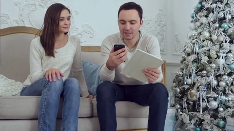 Young couple chilling out on the sofa with the man holding phone and tablet and Video stock 70871228