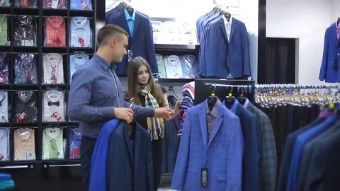 Young couple choose a jacket in the store. Loving guy and girl buy clothes in Stock Footage 75882956