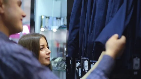 Young couple choose a jacket in the store. Loving guy and girl buy clothes in Stock Footage 76531037