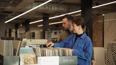 A young couple chooses ceramic tiles from samples at a construction supermarket Stock Footage 301166245