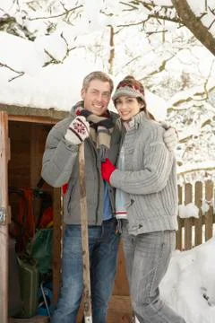 Young couple clearing snow from path to wooden store Stock Photos