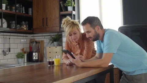 Young couple on a coffee pause in their kitchen are looking something on a ta Stock Footage 117354948