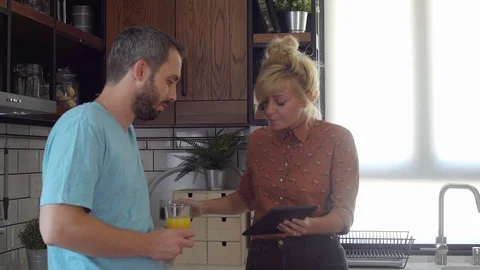 Young couple on a coffee pause in their kitchen are looking something on a ta Stock Footage 117361112