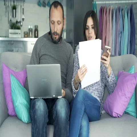 Young couple counting bills on smartphone and laptop sitting on sofa at home Vídeo Stock 69725946