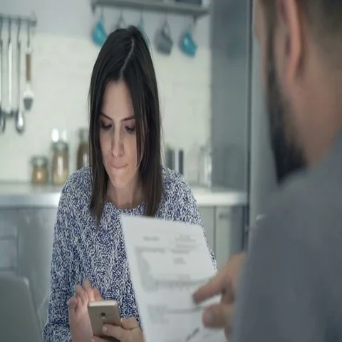 Young couple counting bills on smartphone sitting in kitchen at home Vídeo Stock 69726682