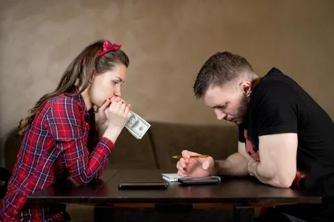 Young couple counts money at the table and looks thoughtfully at the numbers Stock Photos