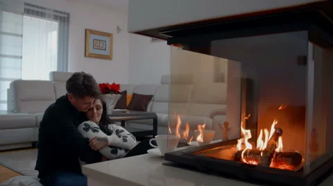 Young couple is cudding in front of the fire-place in their living room Stock Footage