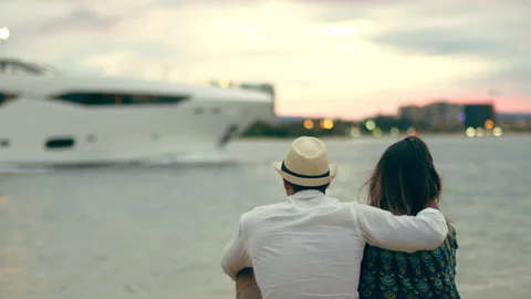 Young couple cuddling on the beach, looking at yacht boating by. Wide shot from Stock Footage 199460183