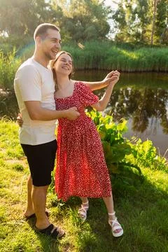 Young couple dancing joyfully by a tranquil river on a sunny summer day Stock Photos