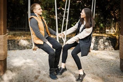 Young couple on a date cute talking while sitting on a swing in the forest among Stock Photos