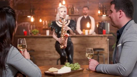 Young couple on a date drinks wine and enjoy saxophone music Stock Footage 106710154