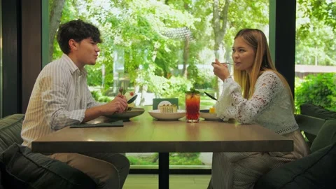  Young couple dining in a restaurant against a backdrop of green trees. Girl Stock Footage 202477691