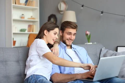 Young couple doing some online shopping at home, using a laptop on the sofa. Stock Photos