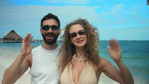 Young couple doing vide call waving hand into the camera behind the blue sea of Stock Footage 291909171