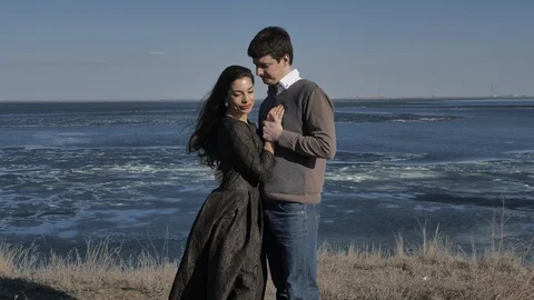Young couple dressed in dark walks along the seashore, sunny day Stock Footage 124749645