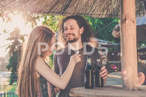 Young couple drinking beer in a bar with afternoon light under bar umbrella. Stock Photos