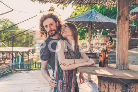 Young couple drinking beer in a bar with afternoon light under bar umbrella. Stock Photos
