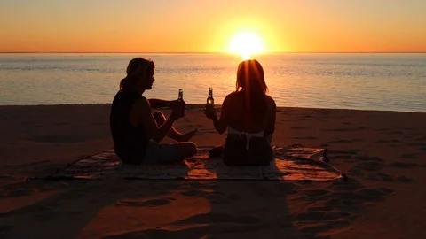 Young couple drinking beer on the beach during summer sunset Stock Footage 114054607