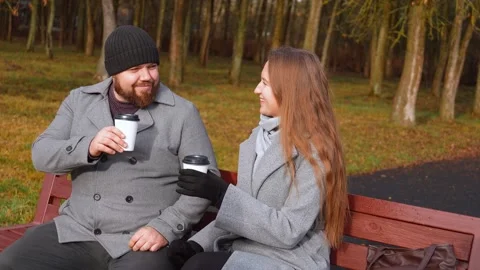 Young couple drinking coffee on a park bench 库存影片 326148954