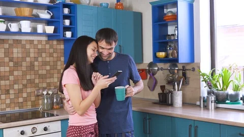 Young couple drinks coffee in kitchen and shopping online using a mobile phone. Stock-Footage 123163220