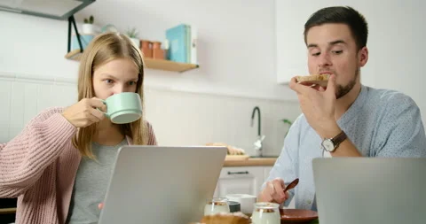 Young Couple Eat Breakfast and Work on Laptops in Kitchen in Home Office Stock Footage