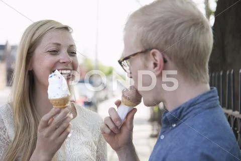 Young Couple Eating Ice Cream Cones On Street