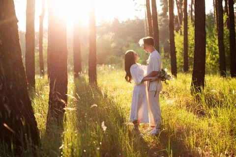 Young couple embracing in a sun-drenched forest with tall pine trees Stock Photos