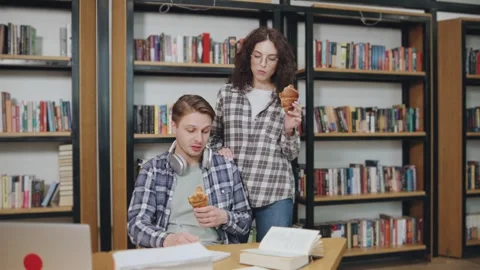 Young couple enjoys snacks while studying in a cozy library surrounded by books Video stock 308667837