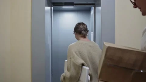 Young couple enters in the elevator with cardboard boxes and folding chair Video stock 150097318