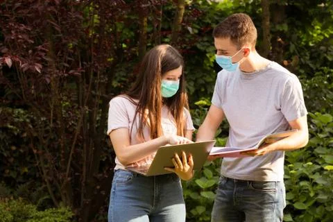 Young couple exchanging data with a laptop in the garden wearing surgical mask. 写真素材
