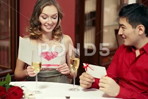 Young couple exchanging Valentines Day greeting cards at restaurant Stock Photos