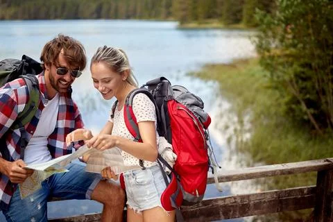A young couple is exploring hiking map while taking a break beside the lake.. Stock Photos