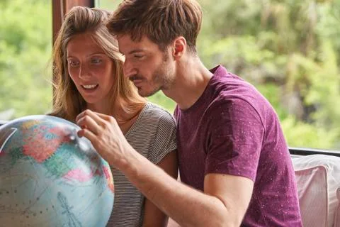 Young couple exploring world globe while sitting on sofa Stockfoto's