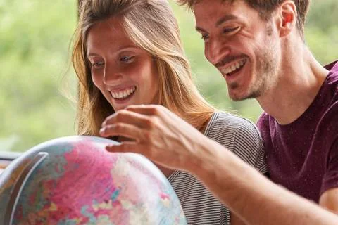 Young couple exploring world globe while sitting in living room Stockfoto's