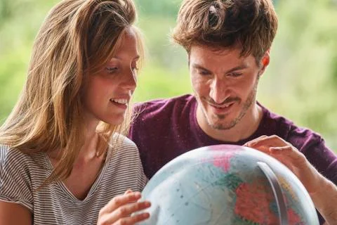 Young couple exploring world globe while sitting in living room Stock Photos