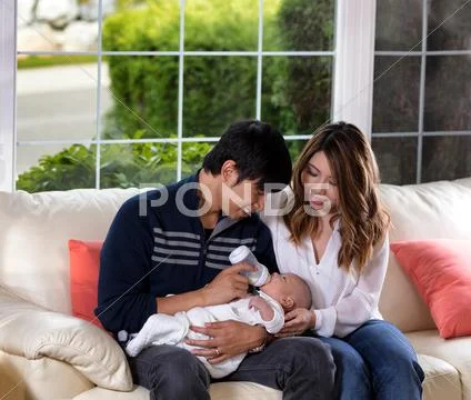 Young couple feeding their infant son on white sofa Stock Photos