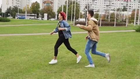 Young couple flirting, man chasing a woman in a city park Stock Footage 83872637
