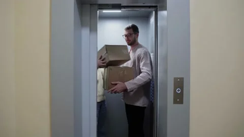 Young couple getting out of the elevator with cardboard boxes and folding chair Video stock 150097745