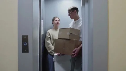 Young couple getting out of the elevator with cardboard boxes and folding chair Video stock 151311735