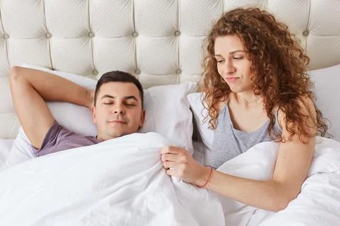 Young couple has marital problems. Displeased female looks under blanket ha.. Stock Photos
