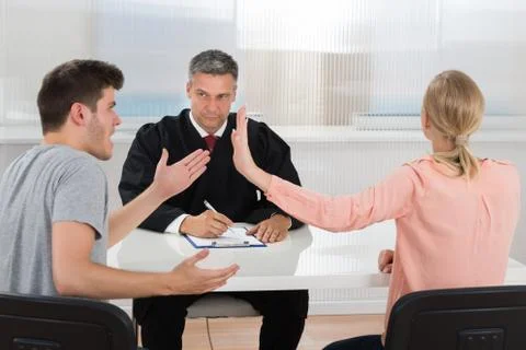 Young Couple Having An Argument In Front Of Male Judge At Desk Stock Photos