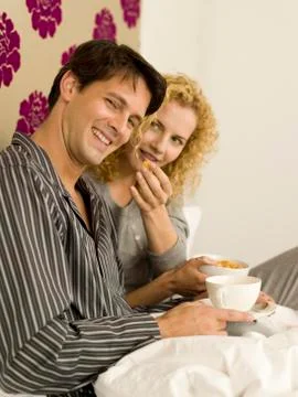 Young couple having breakfast in bed, smiling, portrait Stock Photos